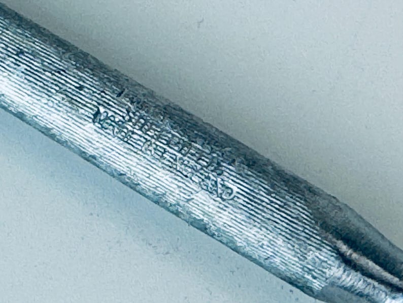 May include: Close-up of a silver metal rod with a textured surface and markings. The rod is about 10 inches long.