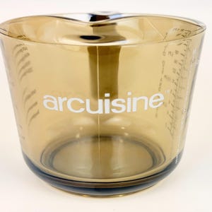 May include: A clear, amber-colored measuring cup with a handle and spout. The word "arcuisine" is printed in white on the front. Measurement markings are visible on the side of the cup.