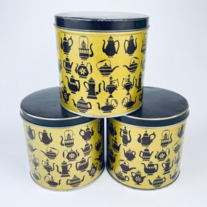 May include: Three vintage metal canisters with black lids and gold bodies. The canisters are decorated with a repeating pattern of black silhouettes of teapots and coffee pots.