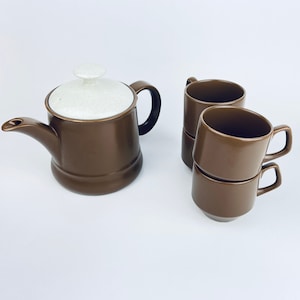 May include: A brown teapot with a white lid and four brown teacups stacked on top of each other.