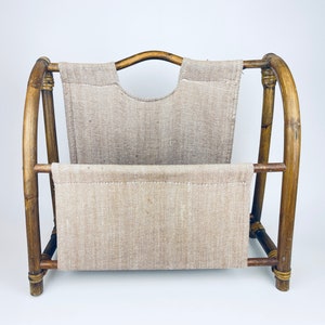 May include: A brown bamboo magazine rack with a beige linen fabric insert. The rack has a simple design with a curved top and a rectangular base.