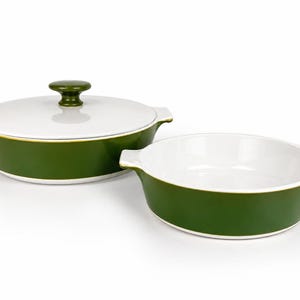 May include: Two round ceramic baking dishes with olive green exteriors and white interiors. One dish features a matching olive green lid with a central knob handle. Both dishes have integrated side handles and a thin gold rim along the top edge.