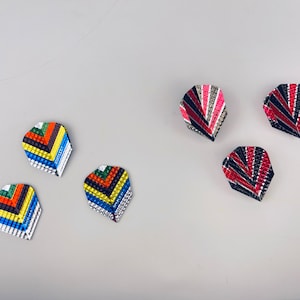 Puede incluir: Seis plumas de dardos coloridas en varios diseños. Las plumas tienen forma de lágrima y presentan patrones de rojo, negro, blanco, azul, rosa y naranja. Las plumas están dispuestas sobre una superficie gris claro.