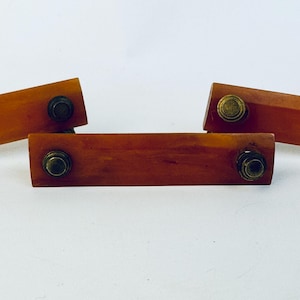 Op de afbeelding: Close-up van een vintage, amberkleurige ladeknop met messingkleurige hardware. De rechthoekige knop heeft aan elk uiteinde twee messingkleurige klinknagels en staat tegen een witte achtergrond. De hardware is waarschijnlijk uit het midden van de eeuw.