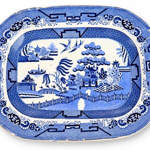 May include: An oval ceramic platter featuring a blue and white willow pattern. The central design depicts a landscape with pagodas, a bridge, a willow tree, and two birds in flight. The wide border is decorated with geometric and floral motifs.