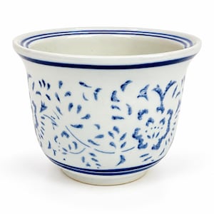 Peut inclure: Un pot de fleurs en céramique blanche avec un bord évasé et un corps arrondi, orné d'un motif floral bleu peint à la main. Le bord présente deux fines lignes horizontales bleues et la surface extérieure affiche des motifs botaniques bleus.