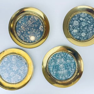 May include: Four round brass picture frames with floral patterned inserts. The frames have a gold finish and a decorative beaded edge. The floral inserts feature a blue background with white flowers.