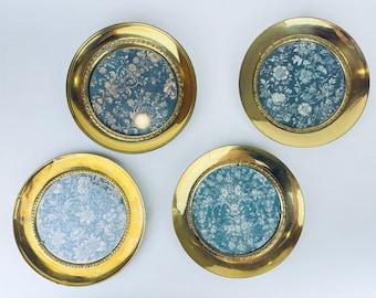 May include: Four round brass picture frames with floral patterned inserts. The frames have a gold finish and a decorative beaded edge. The floral inserts feature a blue background with white flowers.