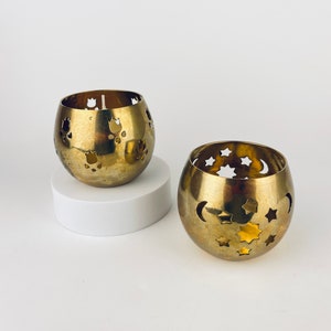 Puede incluir: Dos candelabros de metal dorado con diseños recortados. Un candelabro tiene un diseño de luna y estrellas, el otro tiene un diseño floral.