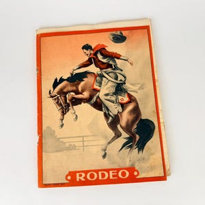 May include: Vintage rodeo print depicting a cowboy on a bucking bronco. The illustration has a warm colour palette with a red border and the word "RODEO" in a red oval at the bottom. The cowboy wears a red scarf and hat.