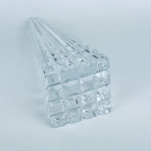 May include: Clear, faceted crystal skewers, arranged in a fan shape. The skewers have a square, geometric design on the handle. The crystal reflects light, creating a sparkling effect. The skewers are on a white background.