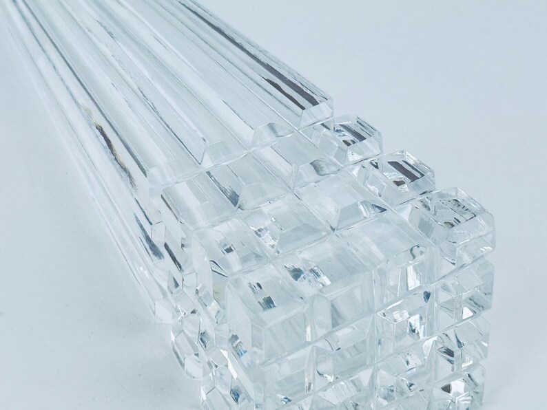 May include: Close-up of a clear, faceted glass object. The object has a geometric design with rectangular and square shapes. The glass is transparent, reflecting light and creating a sparkling effect. The overall theme is decorative.