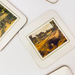 May include: Set of four square coasters with a white background and a gold border. Each coaster features a different vintage painting of a landscape scene. One coaster shows a boat on a river.