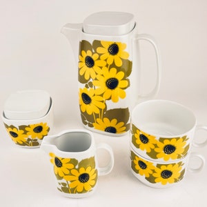 May include: A white ceramic tea set with a yellow and green floral pattern. The set includes a teapot, creamer, sugar bowl, and two cups.