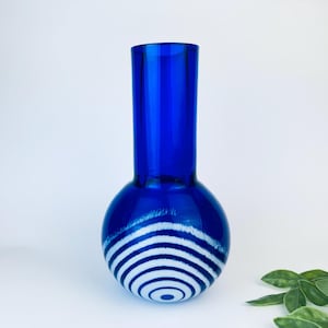 Puede incluir: Una taza de cerámica blanca con un asa negra y el texto "But First, Coffee" en negrita negra. La taza está llena de un líquido oscuro, probablemente café, y se encuentra sobre una superficie clara.