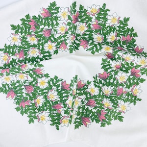 May include: White tablecloth with a pink and white floral wreath design. The wreath is made up of pink flowers and green leaves.