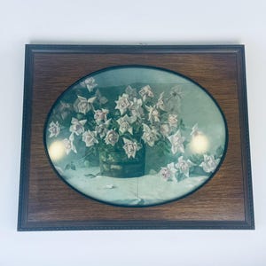 May include: A framed oval print of a still life featuring a bouquet of white roses in a green vase. The roses are arranged in a cluster with their stems extending out from the vase. The background is a light green color.