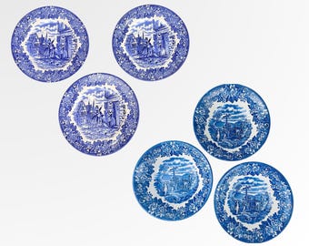 Puede incluir: Seis platos decorativos azules y blancos. Cada plato presenta una escena detallada con figuras y edificios, rodeada por un borde floral. Los platos están dispuestos sobre un fondo blanco, mostrando sus intrincados diseños.