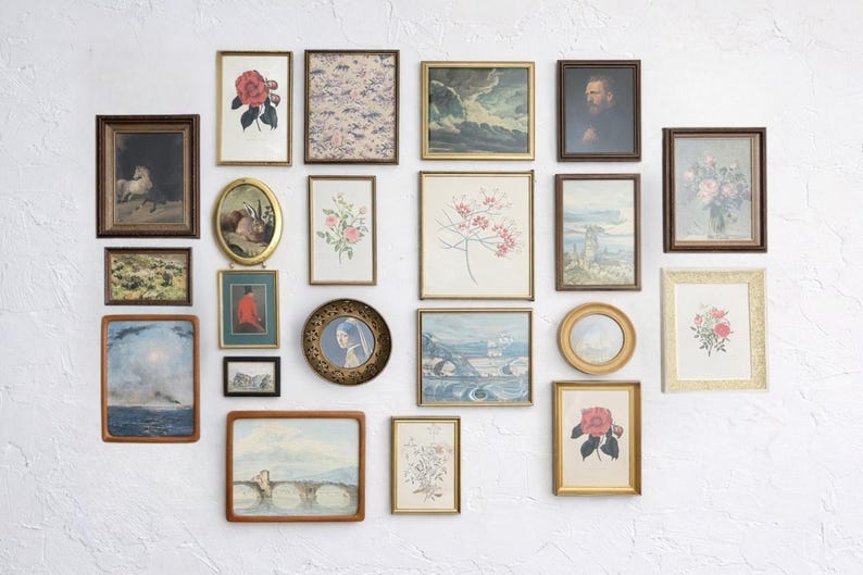 May include: A collection of framed vintage art pieces, including floral prints, landscapes, and portraits, arranged on a white wall. Frames vary in size, shape, and color, with gold, brown, and black frames. The art pieces add a touch of classic decor.