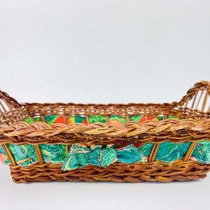 May include: A woven wicker basket with a green and orange floral fabric lining. The basket has a rectangular shape with two handles on the sides.