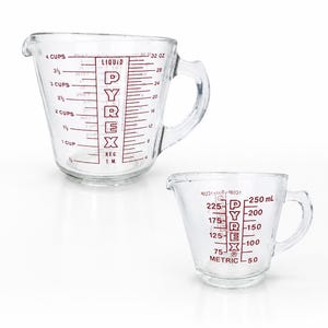 May include: Two clear glass measuring cups with red markings. The larger cup features markings for 1 to 4 cups and 4 to 32 ounces. The smaller cup features metric markings from 50 to 250 ml. Both cups display the Pyrex brand name in red text.