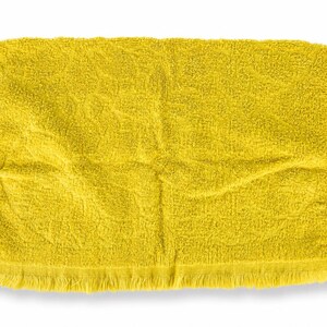 May include: A rectangular yellow towel featuring a textured terry cloth surface and a fringed edge along the bottom. The fabric displays a consistent bright yellow hue with visible folds and a soft, absorbent appearance throughout the entire piece.
