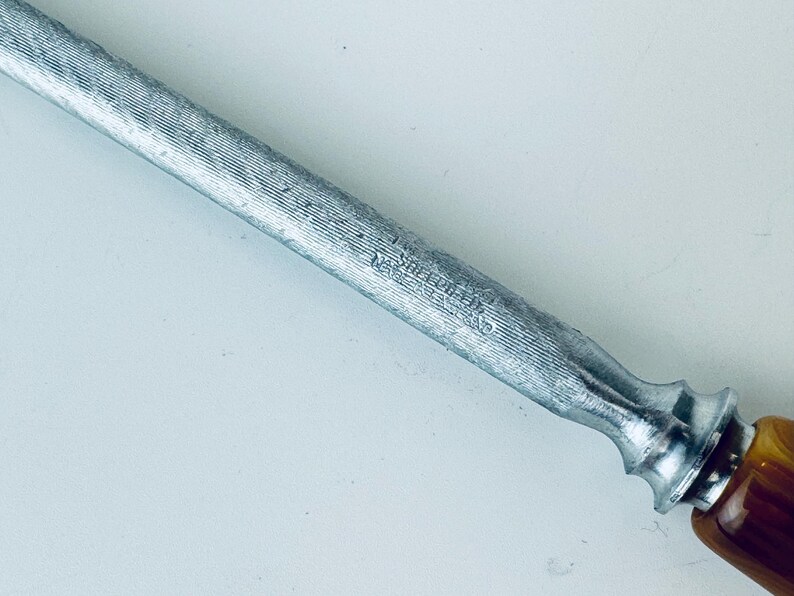 May include: A silver steel knife sharpener with a wooden handle. The sharpener has a textured surface and the words "W&uuml;sthof Trident" are engraved on the side.