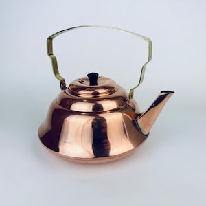 以下が含まれることがあります： 真鍮製の取っ手と蓋に黒いノブが付いた銅製のやかん。やかんは丸みを帯びた広がった形をしています。