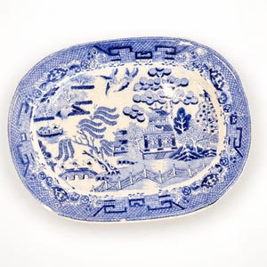 May include: An oval ceramic platter featuring a blue and white willow pattern. The design depicts a landscape with a pagoda, a bridge, willow trees, and birds in flight. The border is decorated with a geometric pattern and circular motifs.