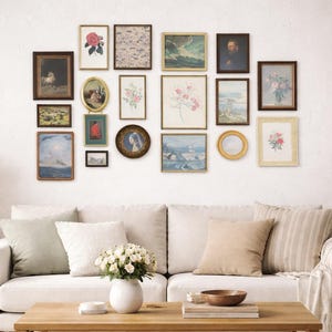 May include: A gallery wall featuring a collection of framed art pieces in various sizes and styles. The frames are in shades of brown, gold, and black, with artwork including landscapes, portraits, and floral designs. The wall is above a white sofa with neutral-colored pillows.