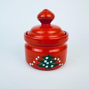 May include: Red ceramic jar with a lid, decorated with a green Christmas tree and white dots.