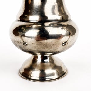 May include: A polished silver-toned metal vase with a rounded, bulbous body, a narrow neck, and a flared circular base. The surface is reflective and smooth, featuring a series of small, evenly spaced circular indentations around the widest part.