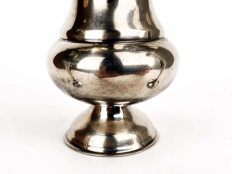 May include: A polished silver-toned metal vase with a rounded, bulbous body, a narrow neck, and a flared circular base. The surface is reflective and smooth, featuring a series of small, evenly spaced circular indentations around the widest part.