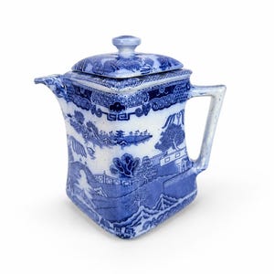 May include: A square-shaped ceramic teapot featuring a blue and white willow pattern. The teapot has a matching lid with a small knob, a pointed spout, and a sturdy handle. The intricate blue transferware design depicts traditional landscape scenes.