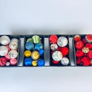 Könnte beinhalten: Ein Set mit sechs Vintage-Weihnachtsbaumschmuckboxen, gefüllt mit einer Vielzahl von bunten Kugeln. Die Kugeln sind aus Satin und haben verschiedene Designs, darunter Sterne, Schneeflocken und den Weihnachtsmann.