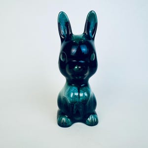 Könnte beinhalten: Eine Keramik-Hasenfigur in Türkis- und Dunkelblautönen. Der Hase hat lange Ohren und einen abgerundeten Körper und sitzt aufrecht. Die glänzende Oberfläche reflektiert das Licht. Ein dekorativer Artikel.