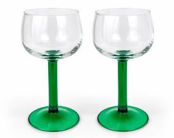 May include: A pair of matching wine glasses featuring clear, rounded bowls supported by vibrant green stems and circular green bases. The glasses have a smooth, polished finish and a classic silhouette, showcasing a clean design with no patterns.