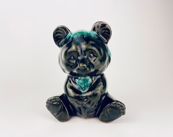 May include: A black ceramic panda bear figurine with green glaze accents. The bear is sitting with its paws tucked in front of it.