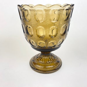 Könnte beinhalten: Eine braune Glasschale auf einem Sockel mit einem gewellten Rand und einem strukturierten, blasenartigen Muster. Die Schale steht auf einem weißen Hintergrund.