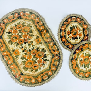 May include: A set of three floral rugs with an oval rug and two round rugs. The rugs feature a cream background with orange and green floral patterns. The edges are trimmed with a gold-colored fringe.