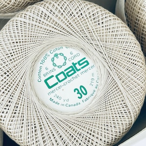 Puede incluir: Carretes de hilo de algodón mercerizado para ganchillo Coats de color blanquecino. La etiqueta dice "Cotton 100%" y "30". Cada carrete contiene 219 m de hilo. El hilo está bien enrollado y listo para tejer.