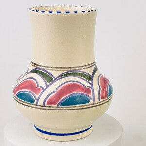 May include: A white ceramic vase with a geometric design in shades of pink, blue, green, and gold. The vase has a wide base and a narrow neck.