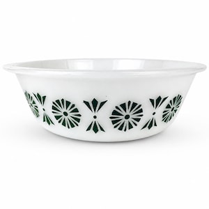 Puede incluir: Un cuenco de cristal blanco con un patrón repetitivo de formas geométricas y motivos florales estilizados en color verde oscuro alrededor del exterior. El cuenco tiene un borde ancho y redondeado con un acabado liso y brillante.