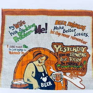 May include: A brown and white tea towel with a humorous illustration of a man drinking beer. The text on the towel reads "My wife has a drinking problem. Me! Beer drinkers make better lovers, but they never remember. Yesterday I gave up drinking, but today I'm making a comeback!"