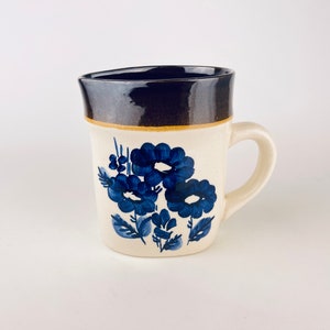 May include: Cream ceramic pitcher with a dark blue rim and handle. The pitcher has a floral design in shades of blue. The flowers and leaves are painted on the front of the pitcher.