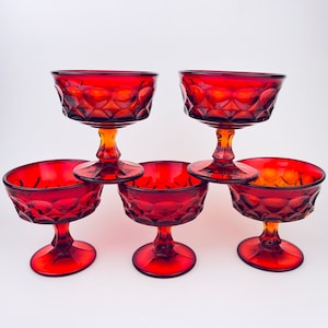 May include: Set of six red glass dessert cups with a diamond pattern. The cups have a clear amber base and are stacked in a pyramid shape.