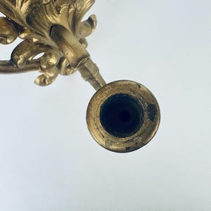 以下が含まれることがあります： 精巧な金色のキャンドルホルダー。詳細なスクロールリーフデザインが施されています。キャンドルホルダーには、キャンドル用の円形の開口部があります。全体的なデザインはヴィンテージで装飾的です。