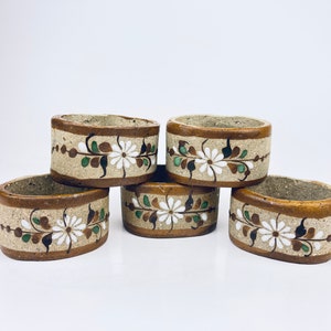 May include: Set of five brown ceramic napkin rings with white and green floral designs.