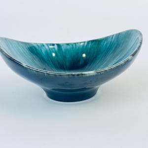 以下が含まれることがあります： 波打つデザインのティールと白のセラミックボウル。ボウルは楕円形で、広く浅いベースがあります。