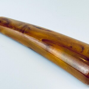 May include: A close-up of a brown and gold bottle opener with a long, smooth handle. The handle is made of a marbled plastic material.